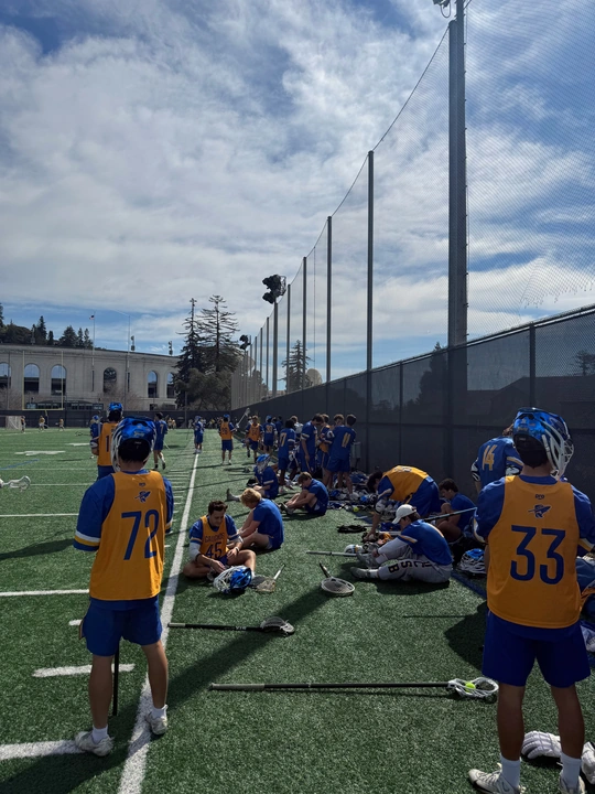 Lacrosse players in blue and gold resting beside the field