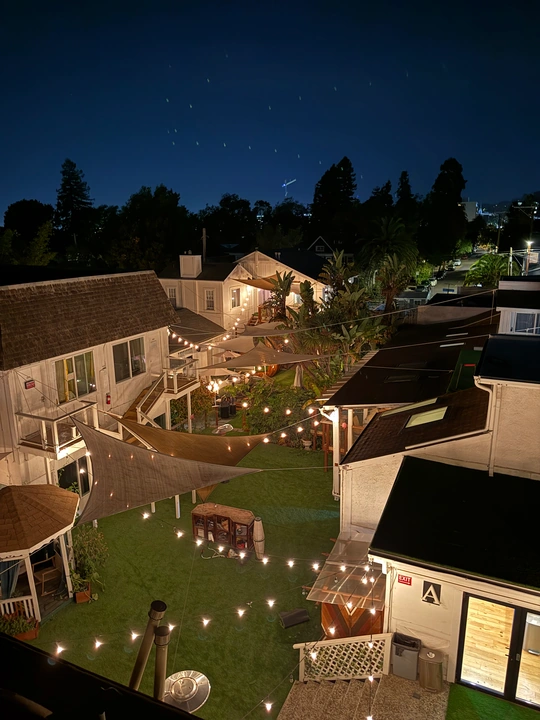 A courtyard at night, with warm string lights between houses beneath a deep blue sky